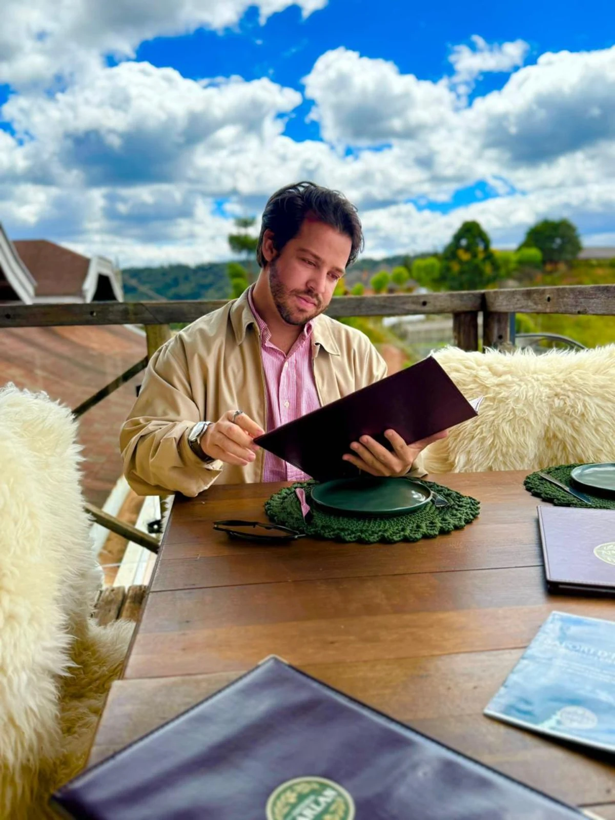 Dieggo Santos lendo o cardápio em uma mesa de restaurante com vista para a serra